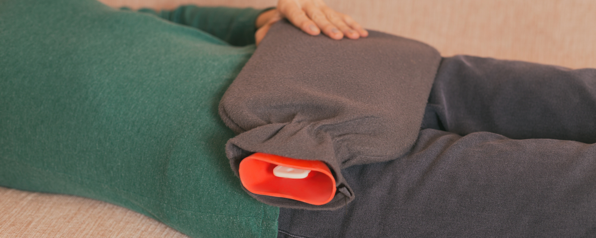 Frau mit Wärmeflasche auf dem Bauch auf der Couch liegend