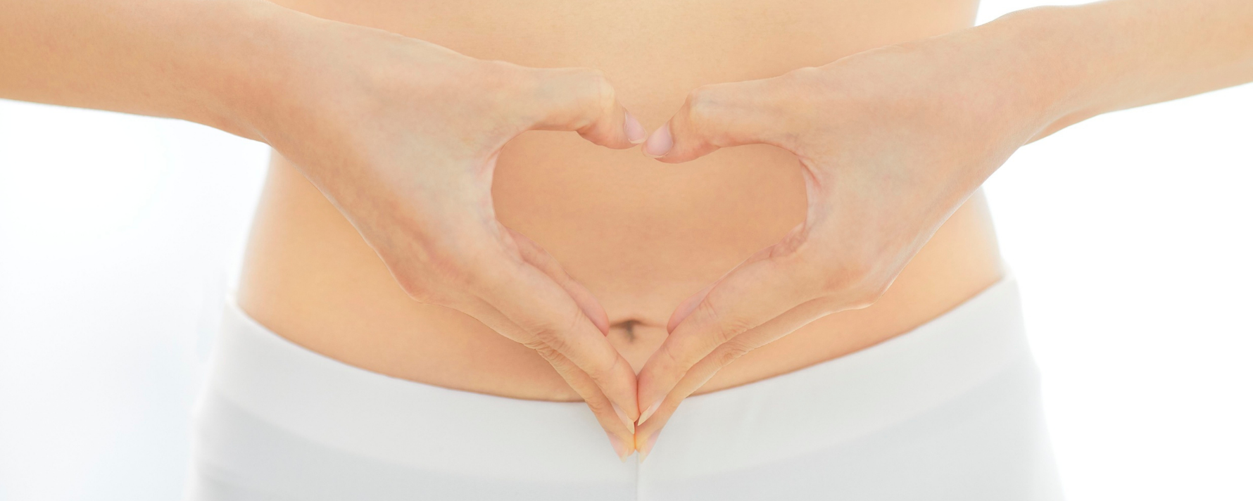 Frau formt mir den Händen ein Herz um ihren Bauchnabel