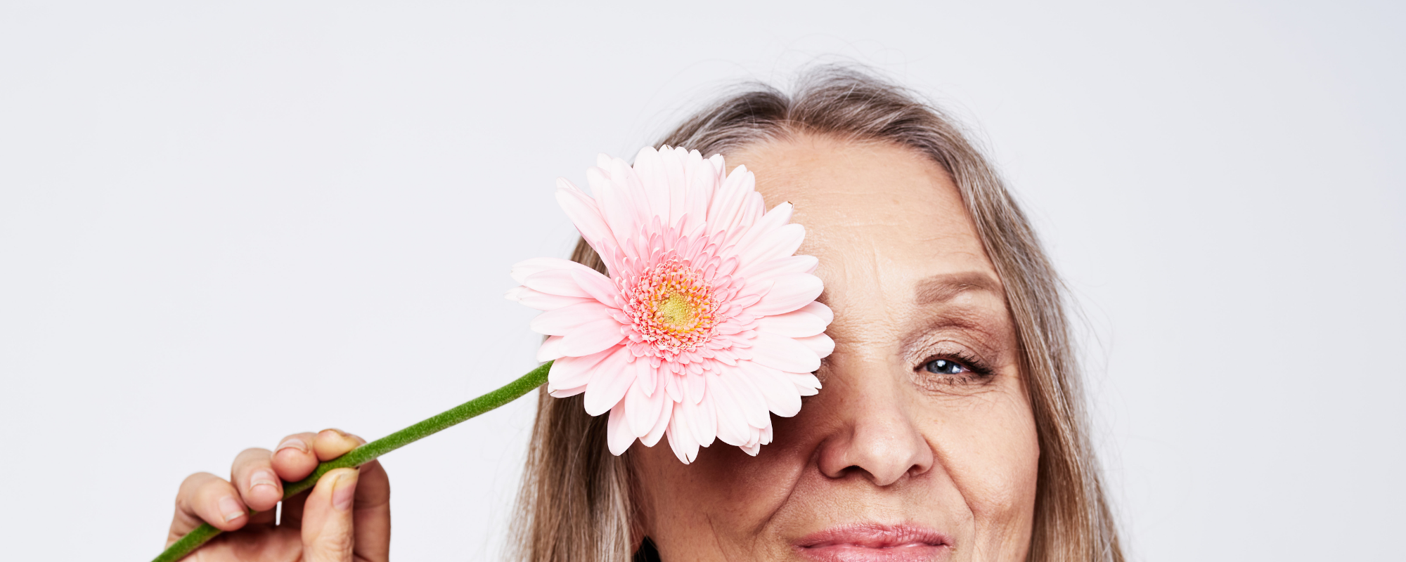 Ältere, schöne Frau mit einer Blume vor dem rechten Auge